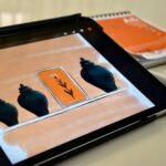 A digital sketch of vases and a flower displayed on a tablet with a stylus and notebook nearby.